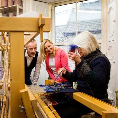 Weaver Lizbeth Mulcahy Dingle demonstrates her loom skills to two onlookers