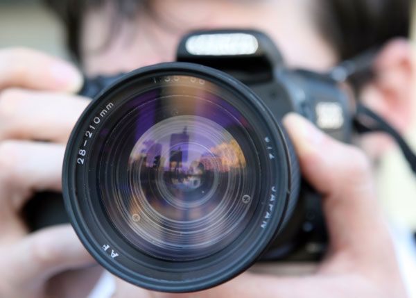 lens of a photographer's camera in foreground with hands and face of person out of focus